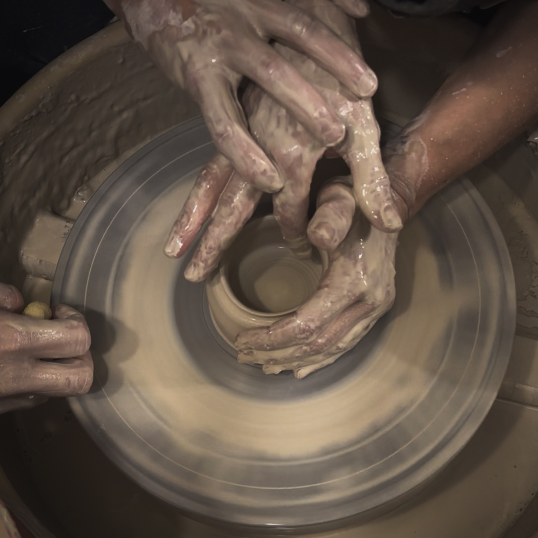 Mani che guidano una corsista nella realizzazione di un pezzo al tornio durante una lezione privata di ceramica.